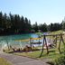 Vorschau: Waldfreibad Gudenhagen Kinderspielgeräte mit Schwimmbecken im Hintergrund